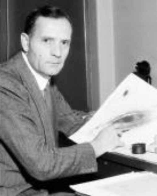 Черно-бяла снимка на мъж в сако, седнал на бюро и разглеждащ фотографска плака.